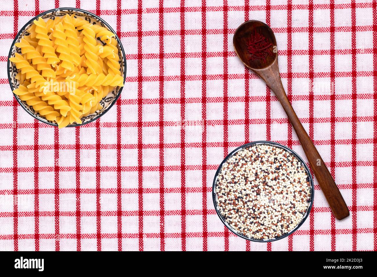 Cibo vegetale. Primo piano di due ciotole con tagliatelle e quinoa e un cucchiaio con fili di spezie safran su una tovaglia. Alimentazione sana. Vista dall'alto con spazio. Foto Stock
