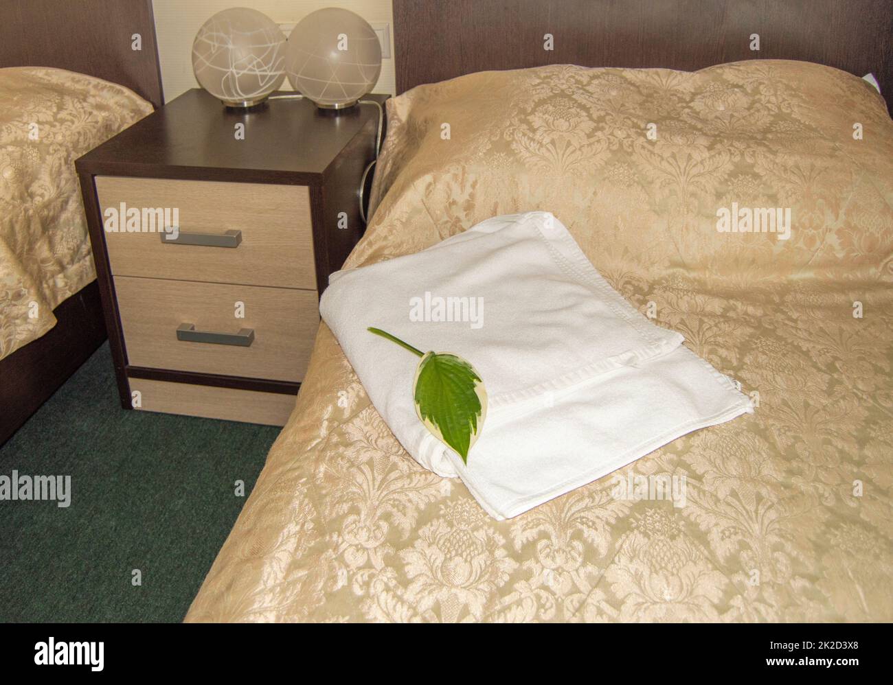 Gli interni di un hotel moderno, un letto con un cuscino e un lussuoso copriletto dorato e asciugamani bianchi, lampade di design sul comodino Foto Stock