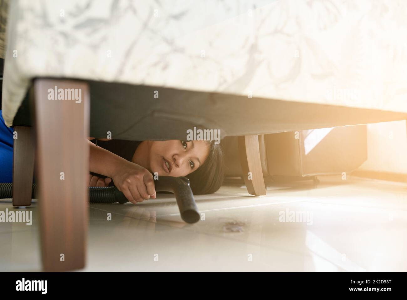 Pulizia di ogni angolo e cranny della casa. Scatto di una donna che aspira sotto un pezzo di mobili. Foto Stock
