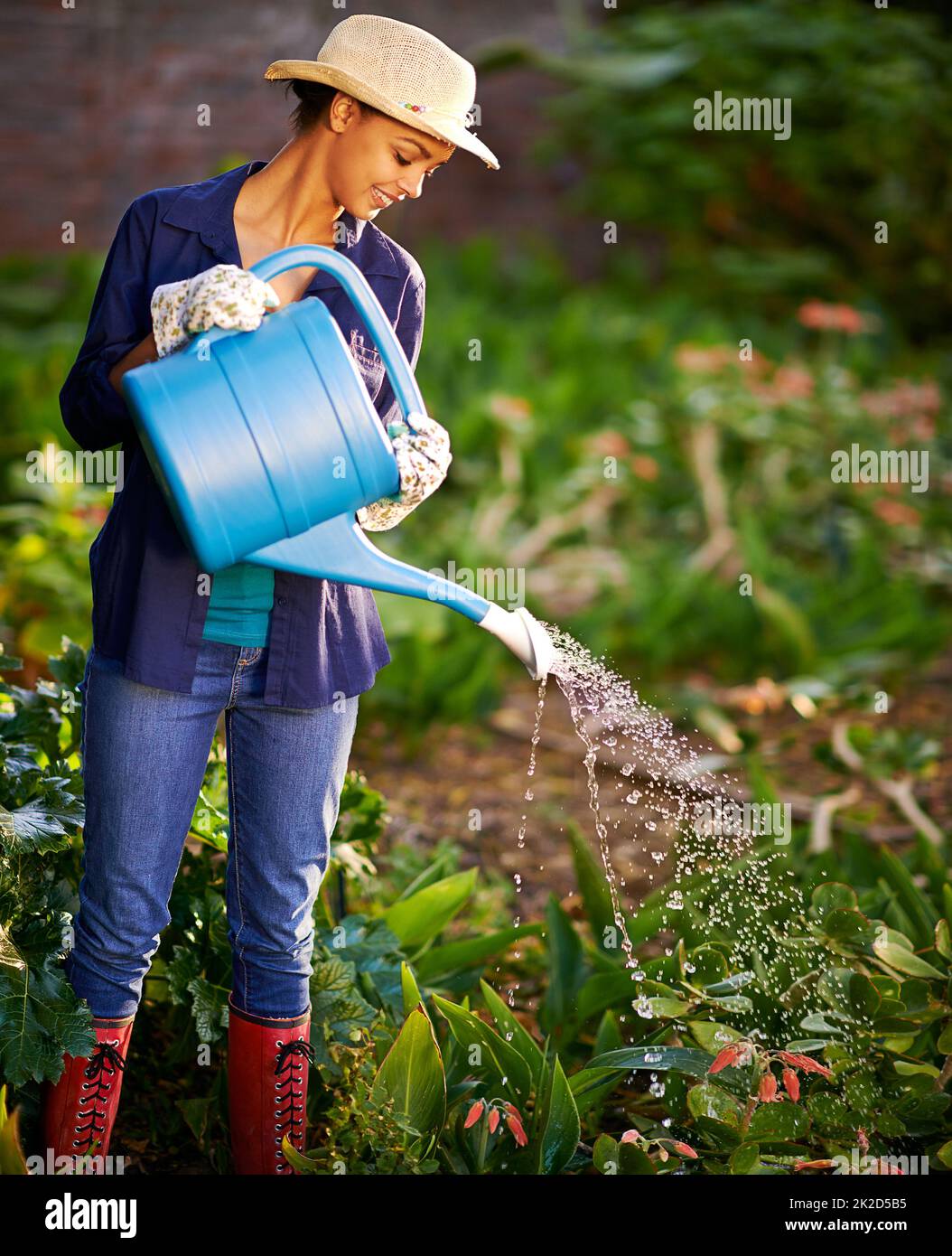 Fai piovere. Scatto di una giovane donna che innaffia il suo giardino. Foto Stock