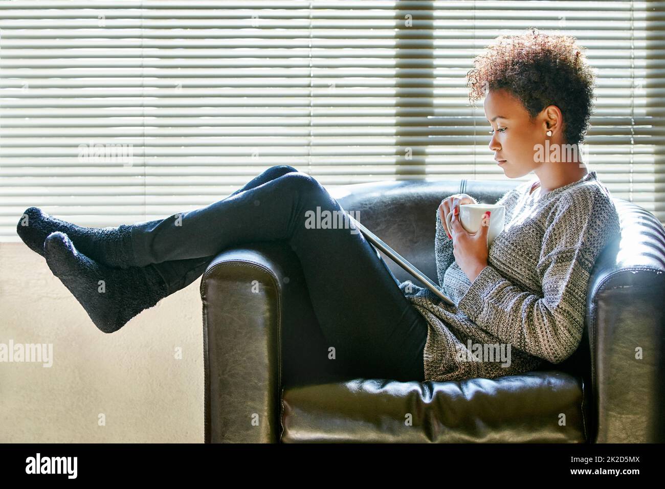 Godendosi il suo tempo libero. Scatto di una giovane donna che si gusta una tazza di caffè e usa un tablet digitale a casa. Foto Stock