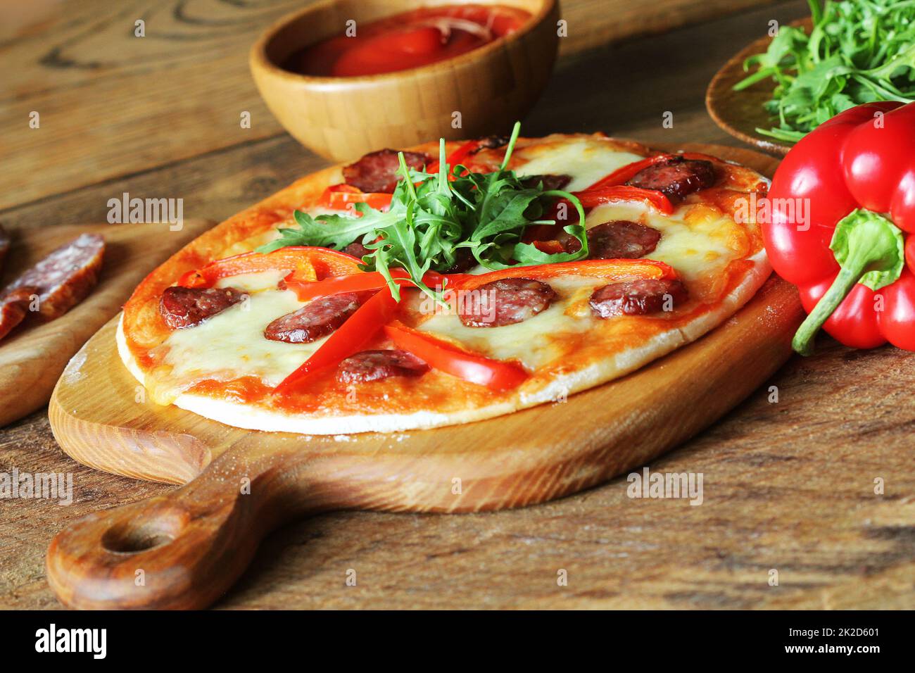 Calda pizza fatta in casa con salsiccia per pizza, paprica, rucola sul tavolo di legno Foto Stock
