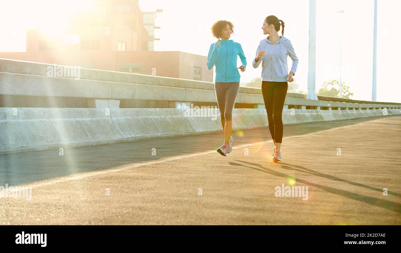 Goditi una corsa mattutina. Scatto di due amici che si jogging insieme in città. Foto Stock