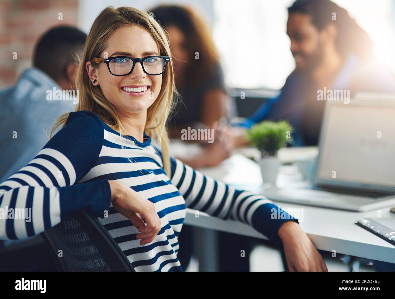 Erano sempre alla ricerca del design da prospettive nuove. Ritratto di un giovane designer seduto in ufficio con i suoi colleghi sullo sfondo. Foto Stock