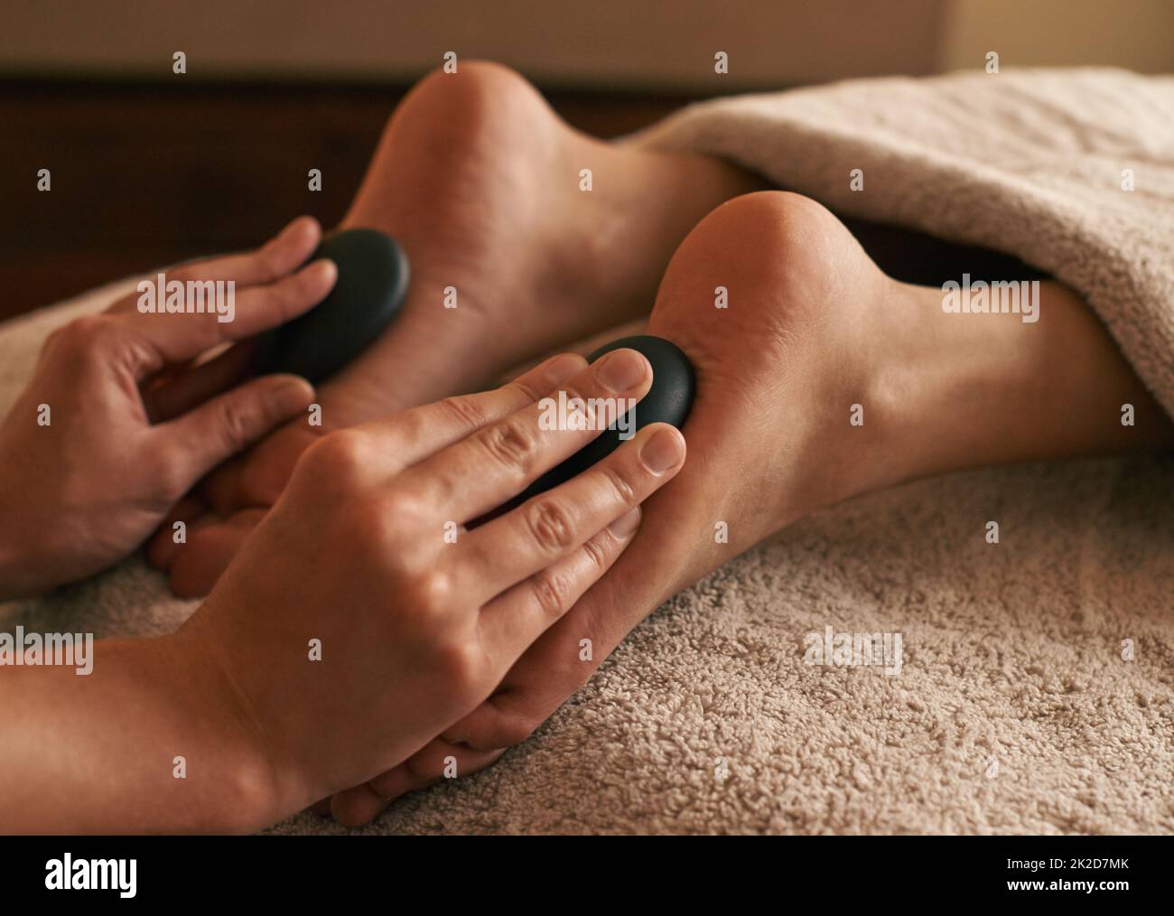 Restauro totale del corpo. Scatto corto di una donna che riceve la terapia calda della pietra sui suoi piedi. Foto Stock