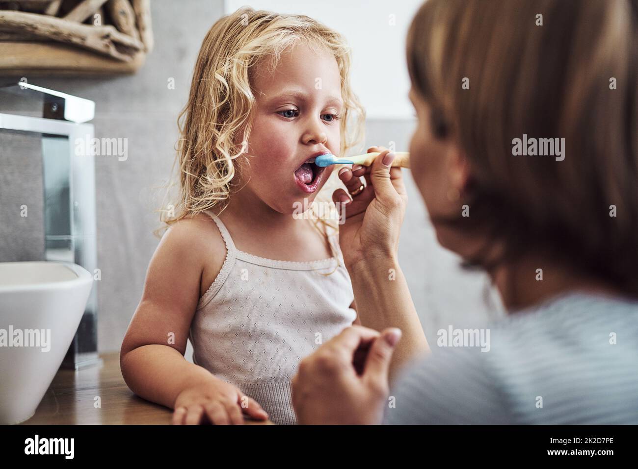Sono io che lo faccio giusto mamma. Scatto corto di una bambina adorabile in piedi e ottenere aiuto da sua madre mentre le spazzolava i denti. Foto Stock