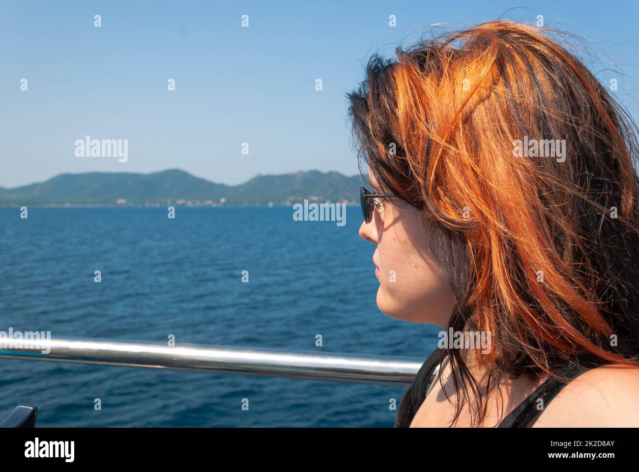Donna con nero arancio seduta su una nave da crociera che guarda al mare Foto Stock