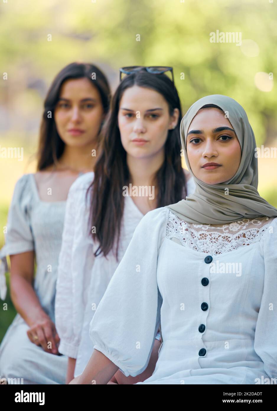 Musulmano, islam e moda con una donna islamica seduta fuori con i suoi amici in fila durante il giorno. Religione, fede e credenza con un arabo Foto Stock