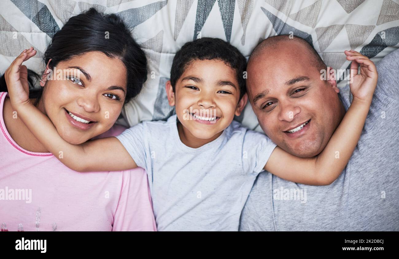 Questi sono i miei migliori amici. Ritratto di una giovane famiglia allegra che si stende giù e che si stende a letto sorridendo tutto il senso a casa durante il giorno. Foto Stock