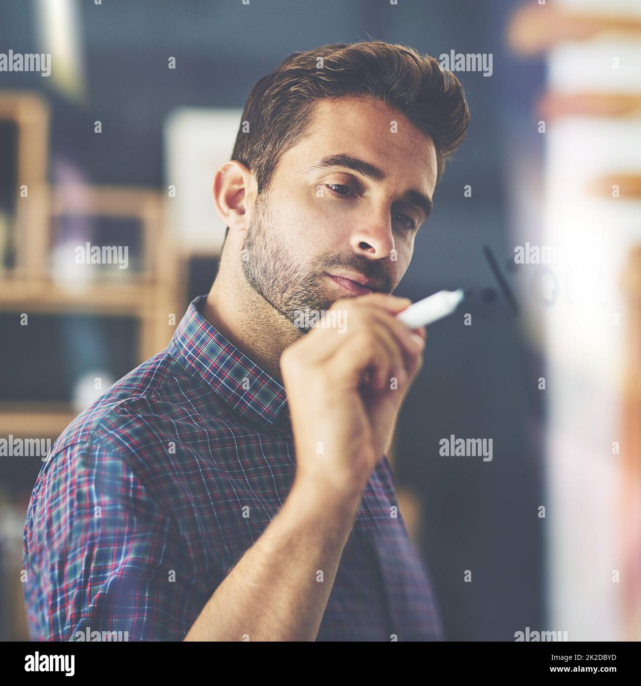 Gli scritti sul muro.... Scatto di un bel giovane uomo d'affari che scrive le note su una parete di vetro in un ufficio. Foto Stock