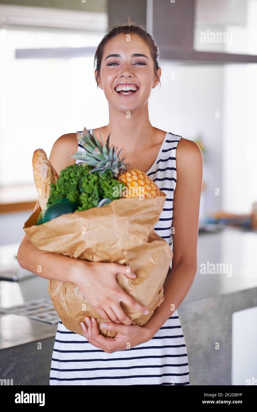 Una vita sana è una vita felice. Una donna attraente che tiene una borsa di generi alimentari in cucina. Foto Stock