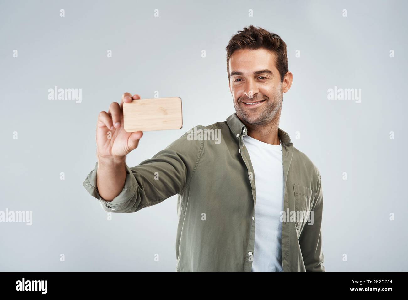 Tempo selfie. Studio girato di un giovane allegro che prende un autoritratto con il suo cellulare mentre si trova su uno sfondo grigio. Foto Stock