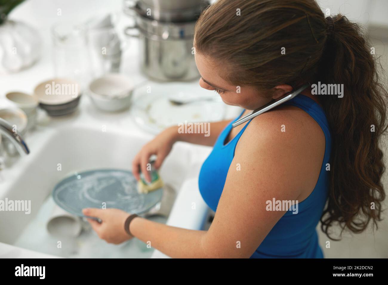 Il multitasking è una seconda natura per lei. Shot di una donna che parla su un cellulare mentre lavano piatti. Foto Stock