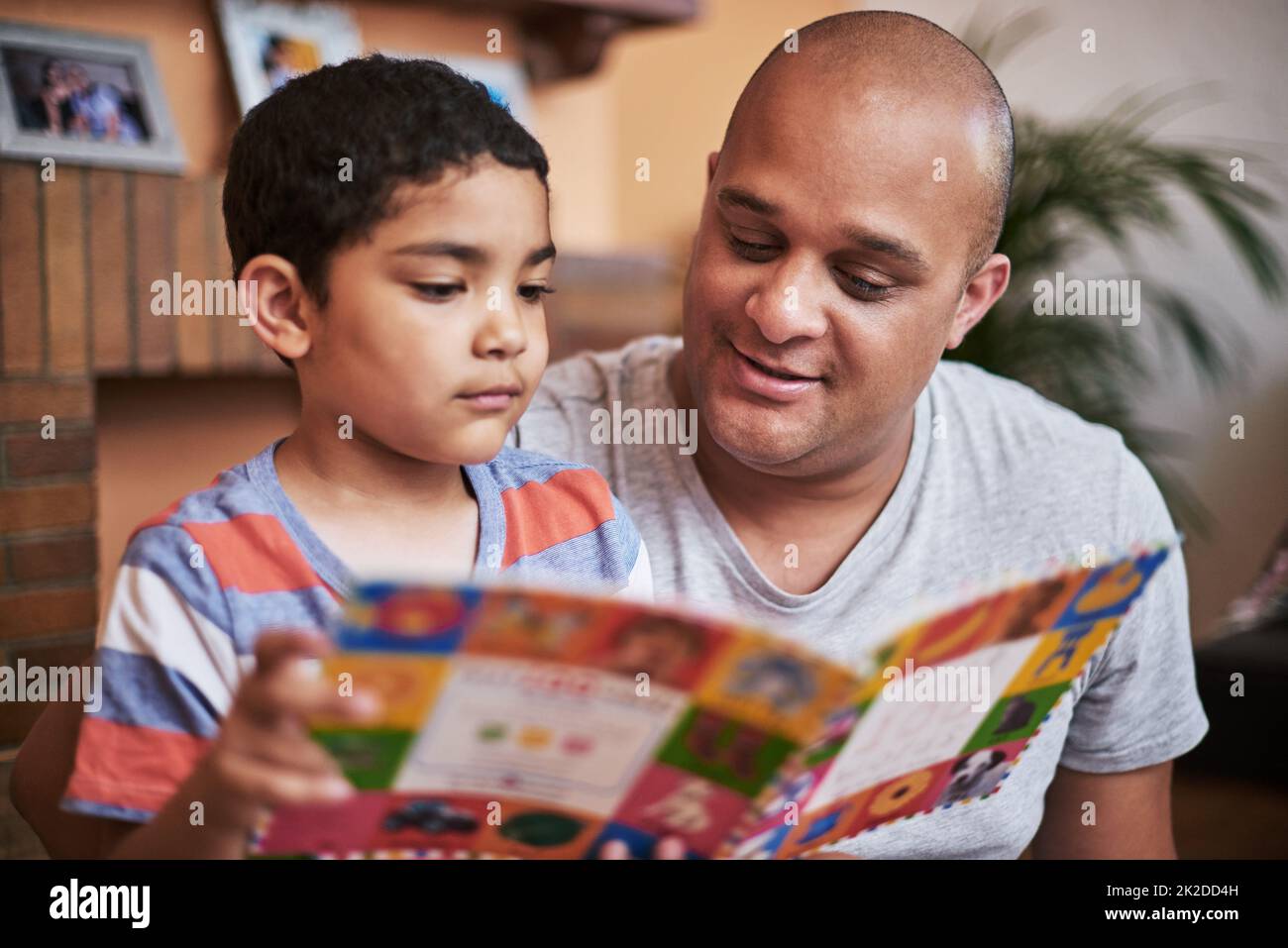 Ora il suo turno di leggere. Scatto corto di un ragazzino allegro e suo padre che legge un libro di storia insieme a casa durante il giorno. Foto Stock