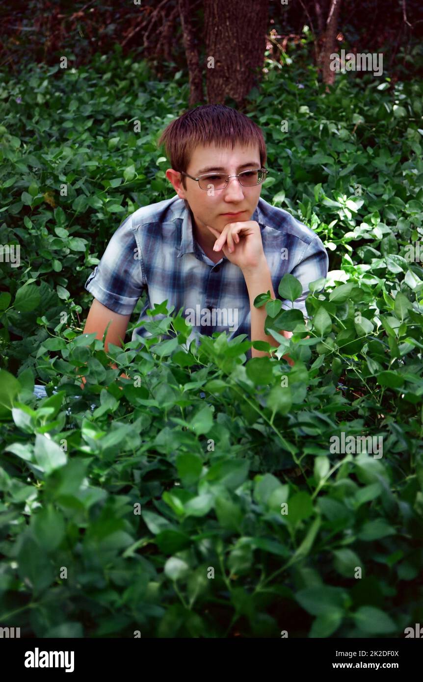 Giovane uomo circondato da piante verdi pensare Foto Stock