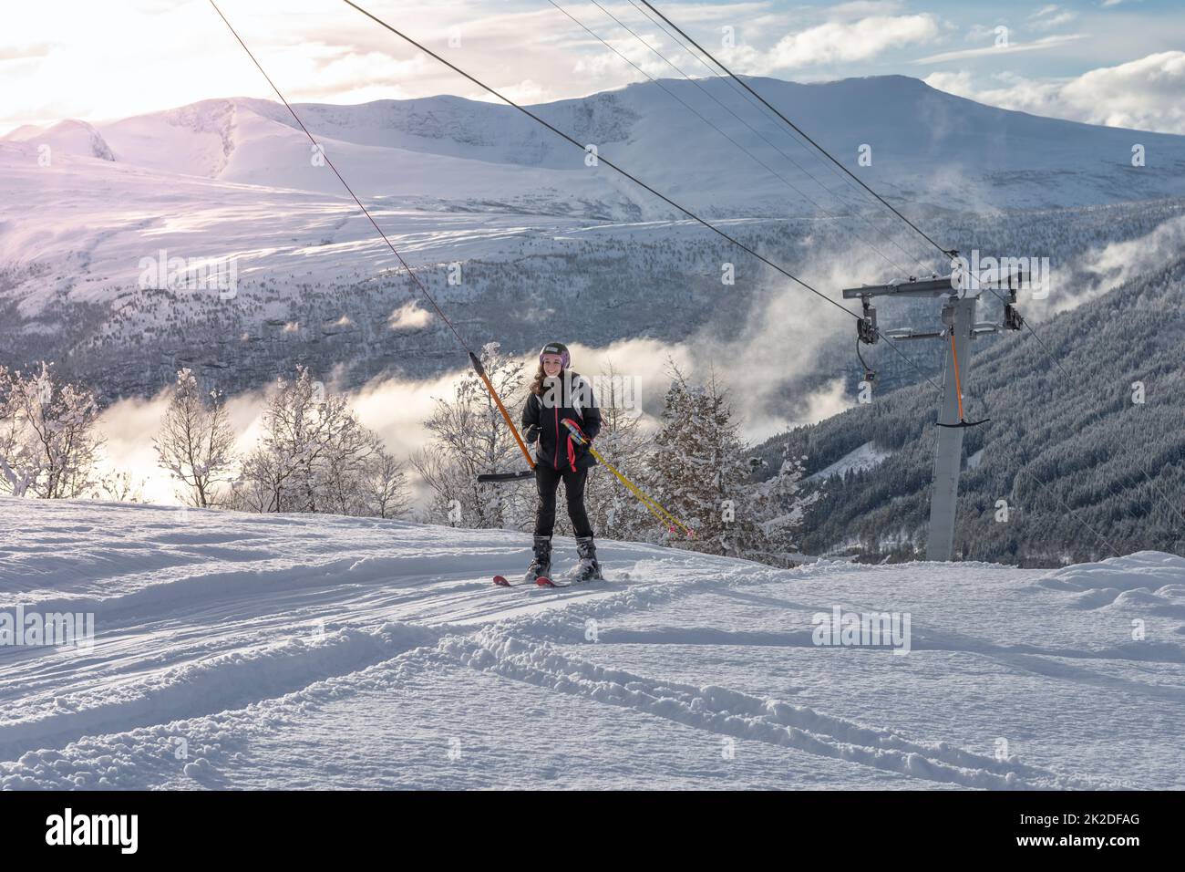 Donna con capelli castani e abbigliamento da sci nero con ski lift Foto Stock