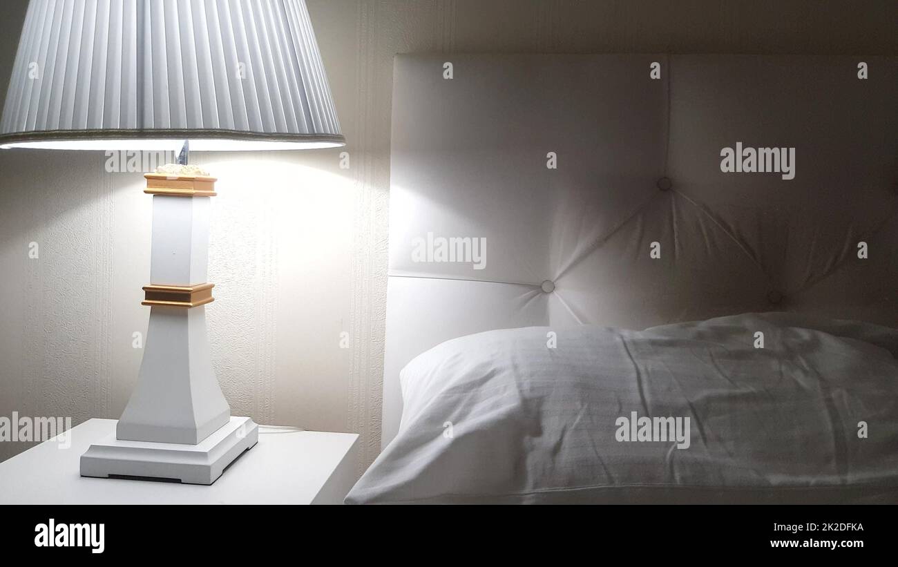 Letto d'albergo di lusso, preparazione per il letto, comodino con lampada e lenzuola bianche pulite sul letto con cuscino, sera Foto Stock
