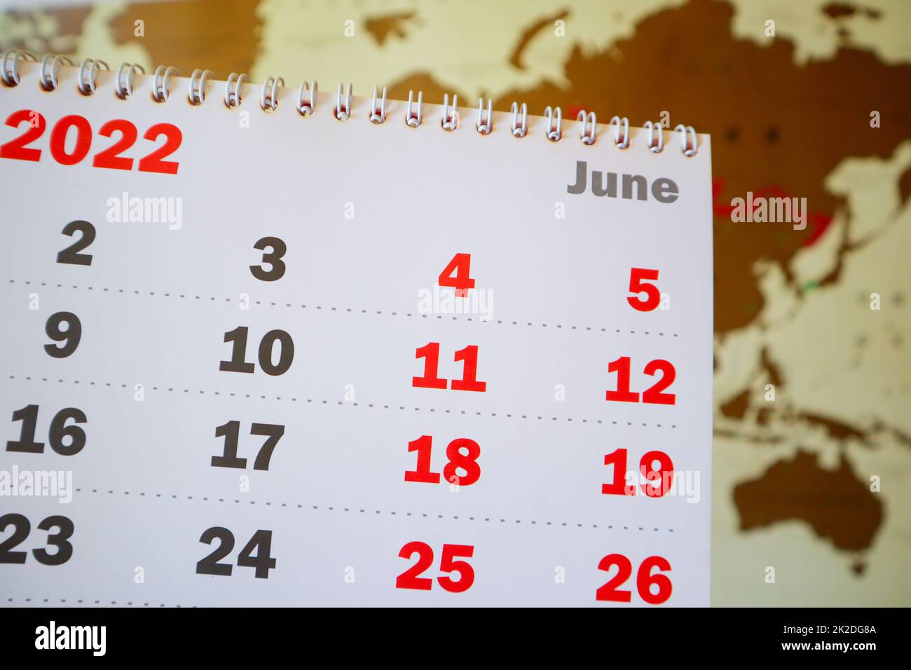 Primo piano di una pagina di un calendario cartaceo con una spirale per il mese di giugno per il 2022 sullo sfondo di una mappa mondiale. Il concetto di pianificare una vacanza estiva e un viaggio d'affari Foto Stock