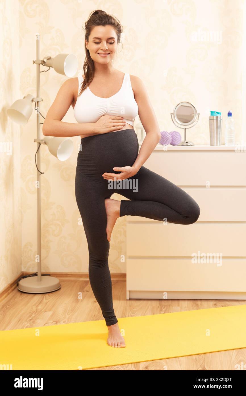 Donna incinta durante il suo orto yoga a casa Foto Stock
