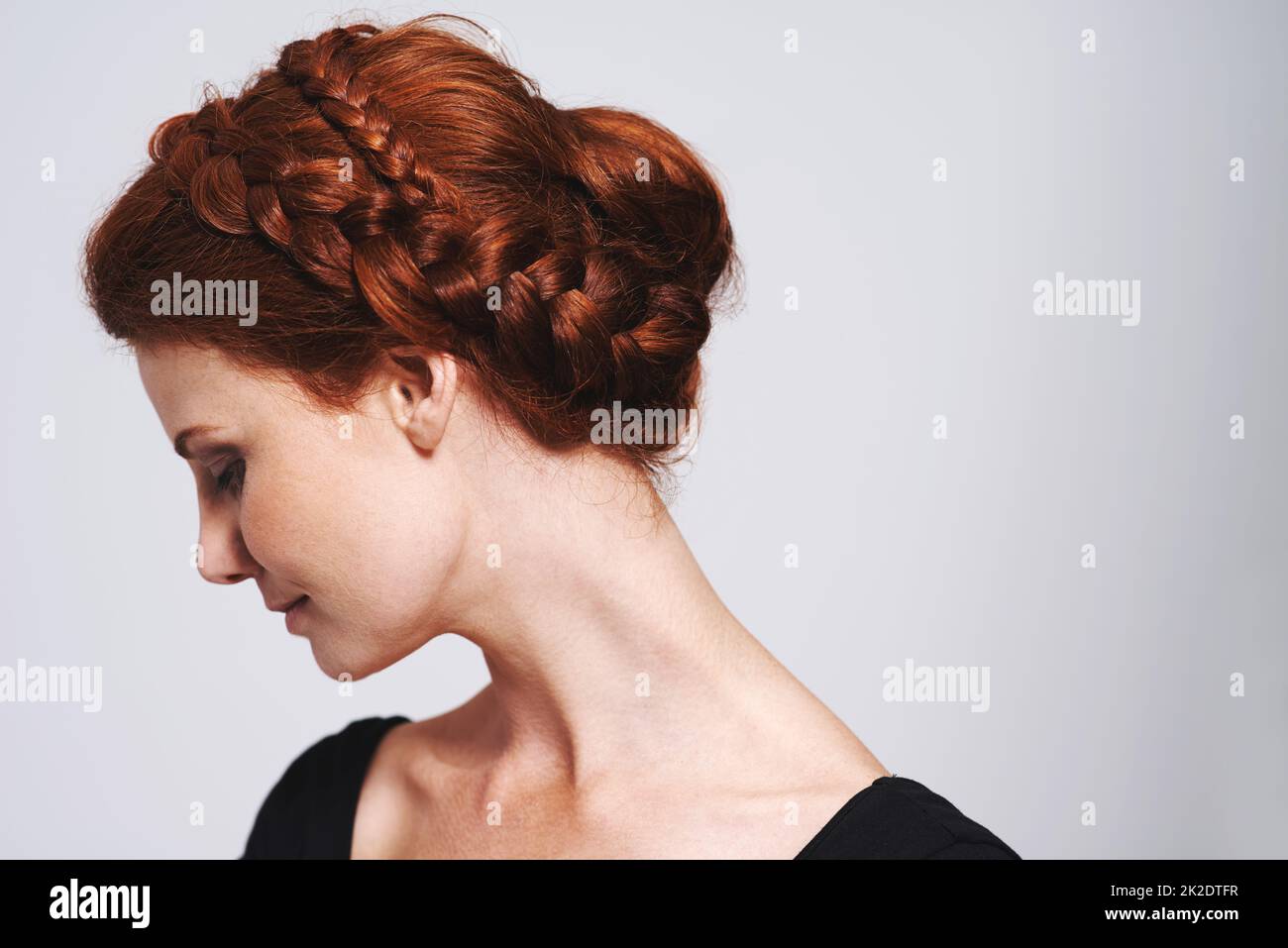 Morbido e romantico. Studio girato di una bella donna rossa con un intrecciato up-do posando su uno sfondo grigio. Foto Stock