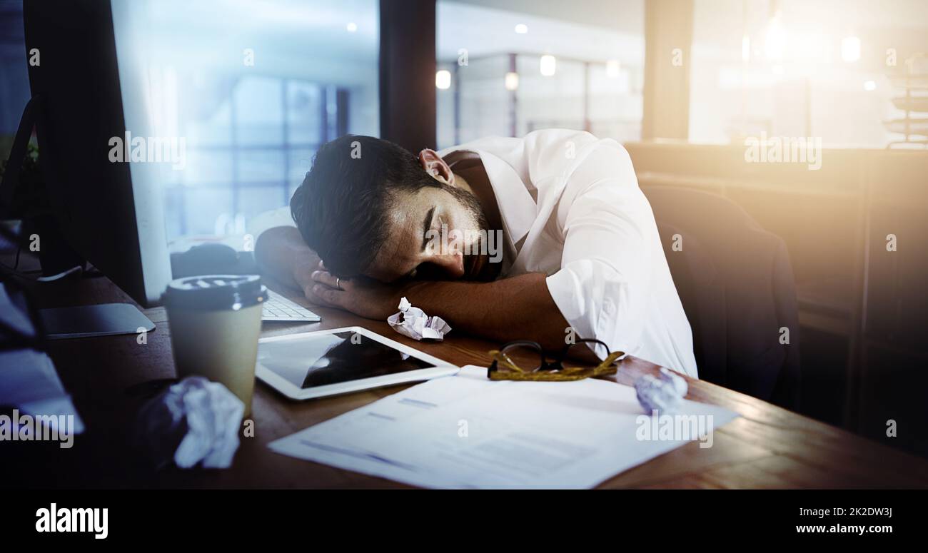 HES lo chiamò una notte. Scatto corto di un bel giovane uomo che dorme alla sua scrivania mentre lavorava tardi in ufficio. Foto Stock