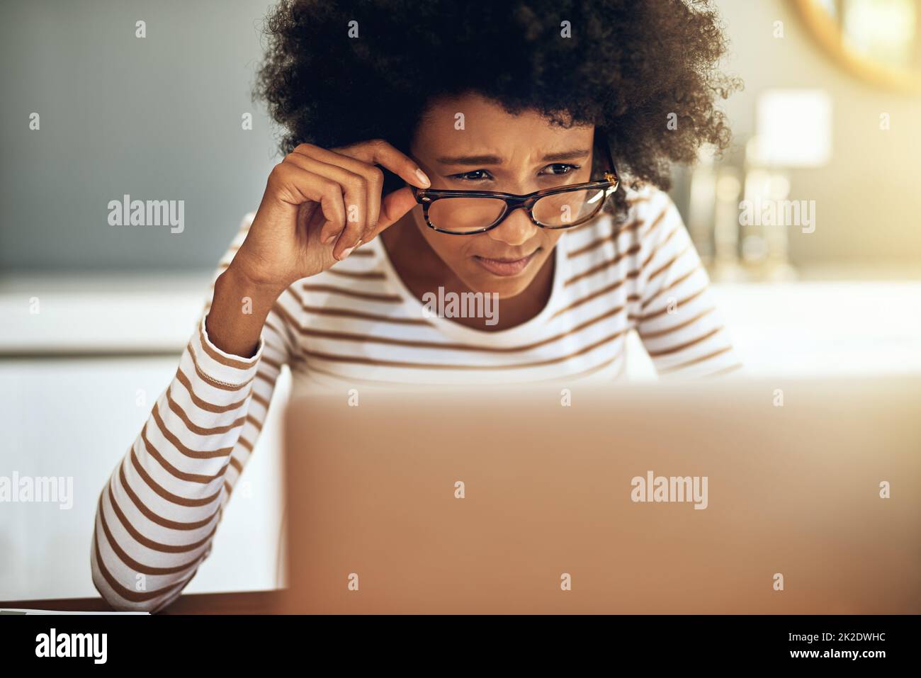 Lo leggo correttamente. Scatto di una giovane donna focalizzata che lavora sul suo laptop mentre tiene i suoi occhiali da lettura a casa durante il giorno. Foto Stock