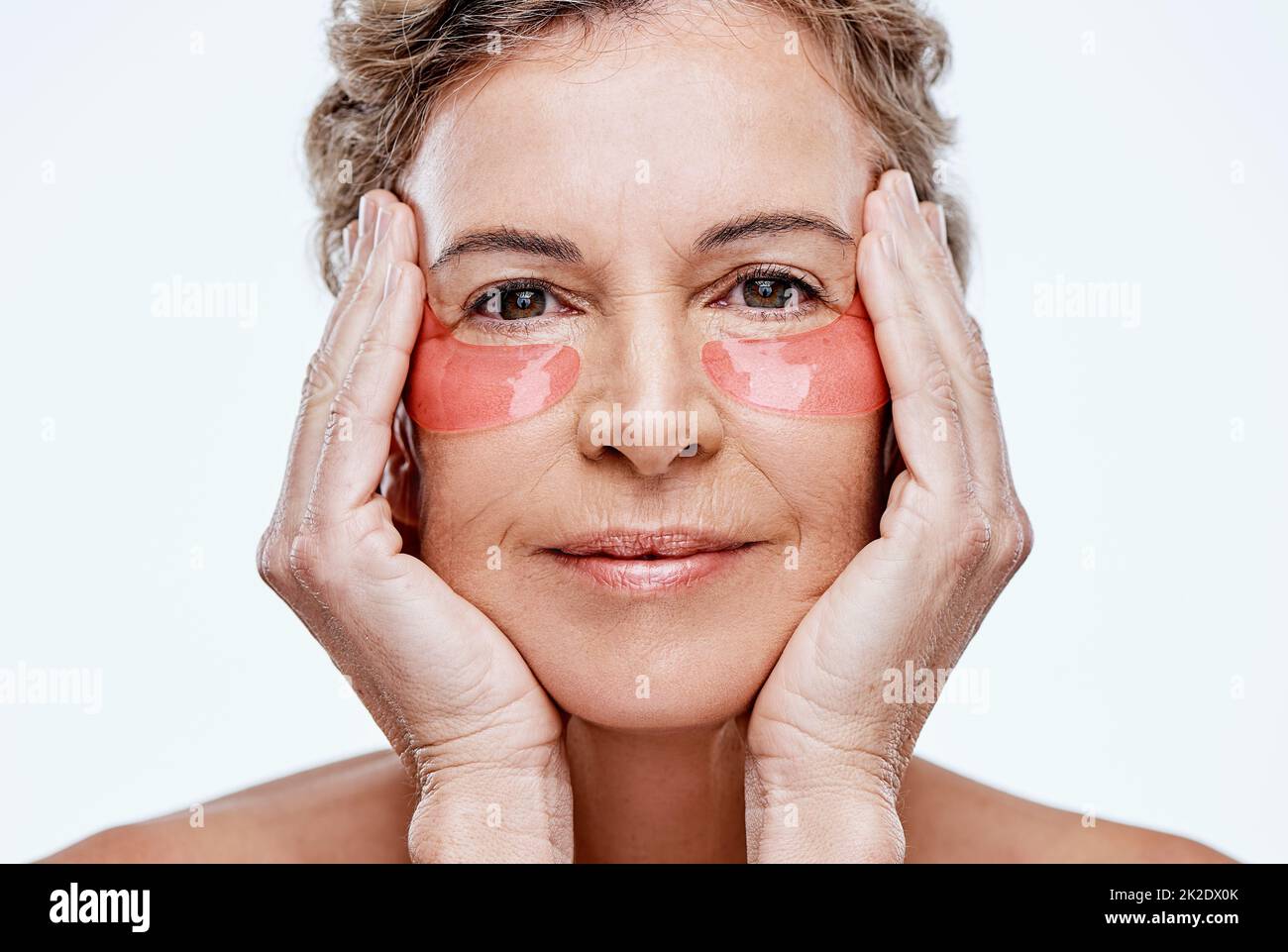 Prendendosi cura della vostra pelle la manterrà più giovane per più lungamente. Foto di una donna matura che indossa delle macchie di gel sotto gli occhi mentre si posa su uno sfondo bianco. Foto Stock