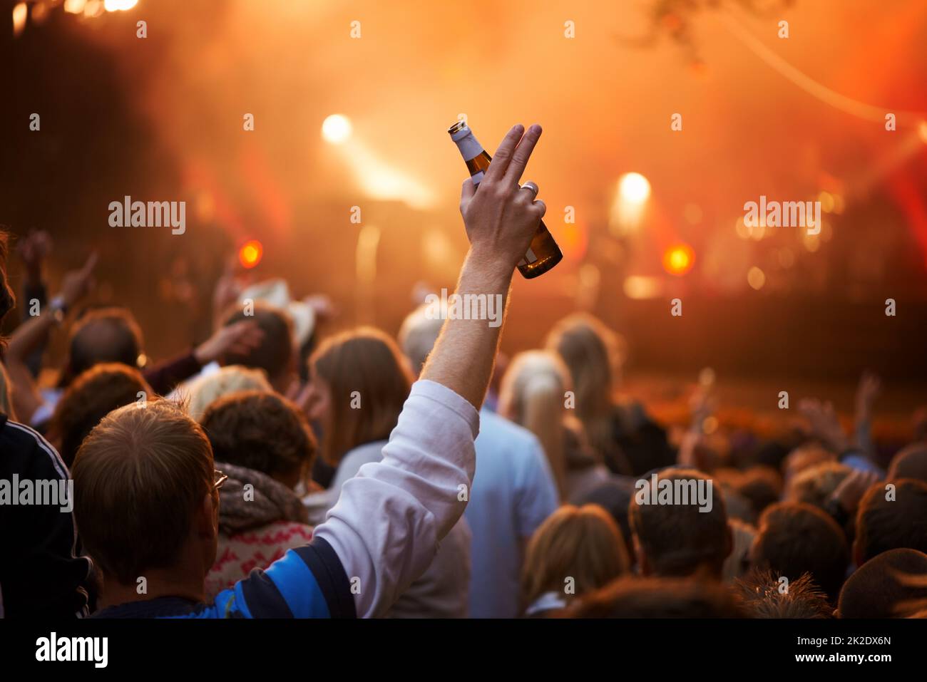 Saluto. Vista posteriore di un ragazzo in un pubblico che saluta la band sul palco di un festival musicale. Foto Stock