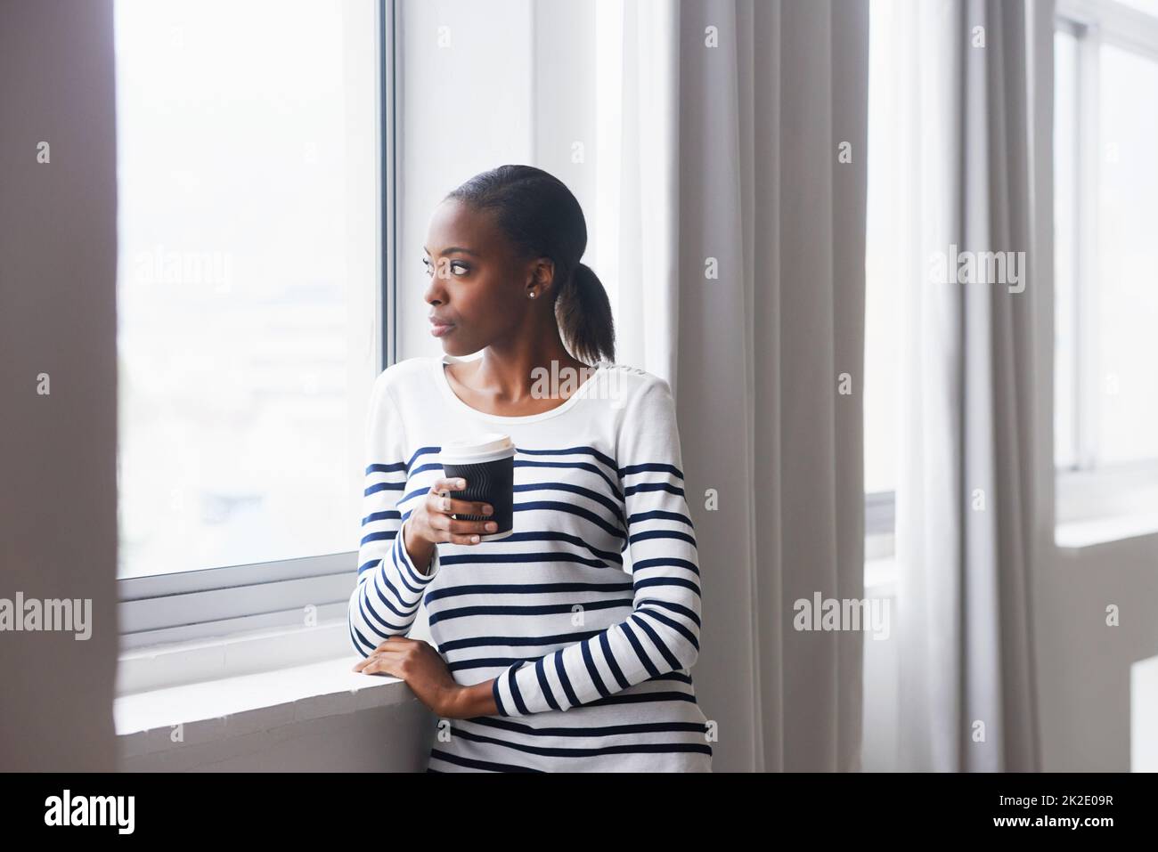 Che cosa sono i vicini fino ad ora. Una giovane donna pensierosa che guarda fuori da una finestra sulla sua pausa caffè. Foto Stock