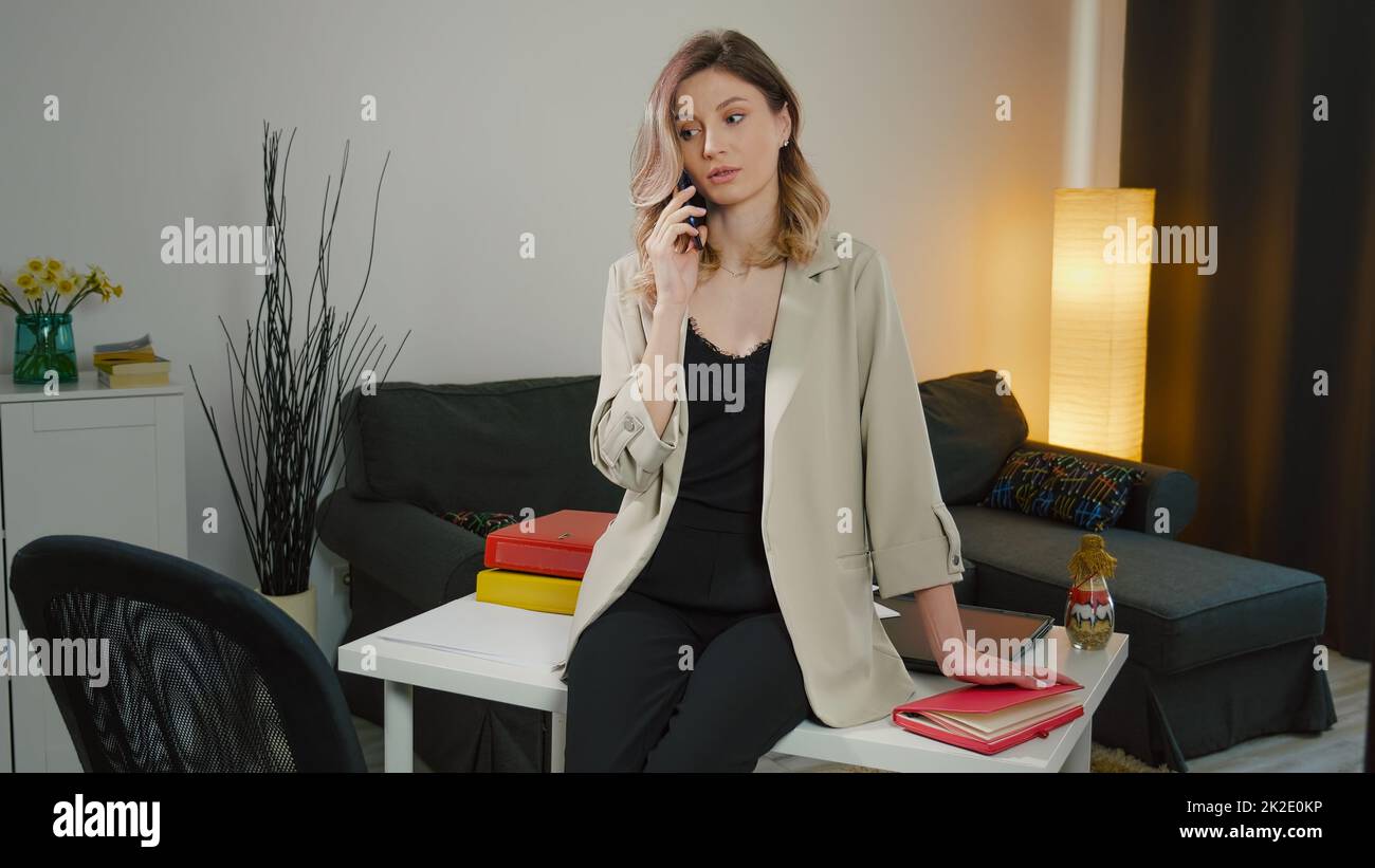 Arrabbiato caucasica donna d'affari spiegare al telefono. Si siede sulla scrivania, è sconvolta, ha una conversazione telefonica. Foto Stock