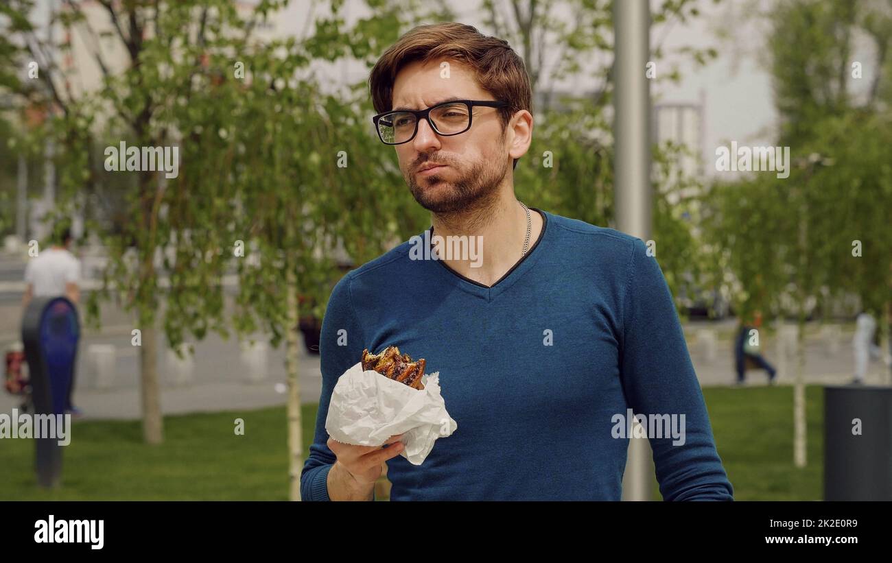 Affollato uomo d'affari pranzo mangiare snack. Dipendente che prende lavoro in pausa. Mangiare snack a piedi. Allegro uomo d'affari che ha pranzo pausa all'aperto. L'uomo affamato mangia. Un giovane frettoloso ha pranzato. Foto Stock