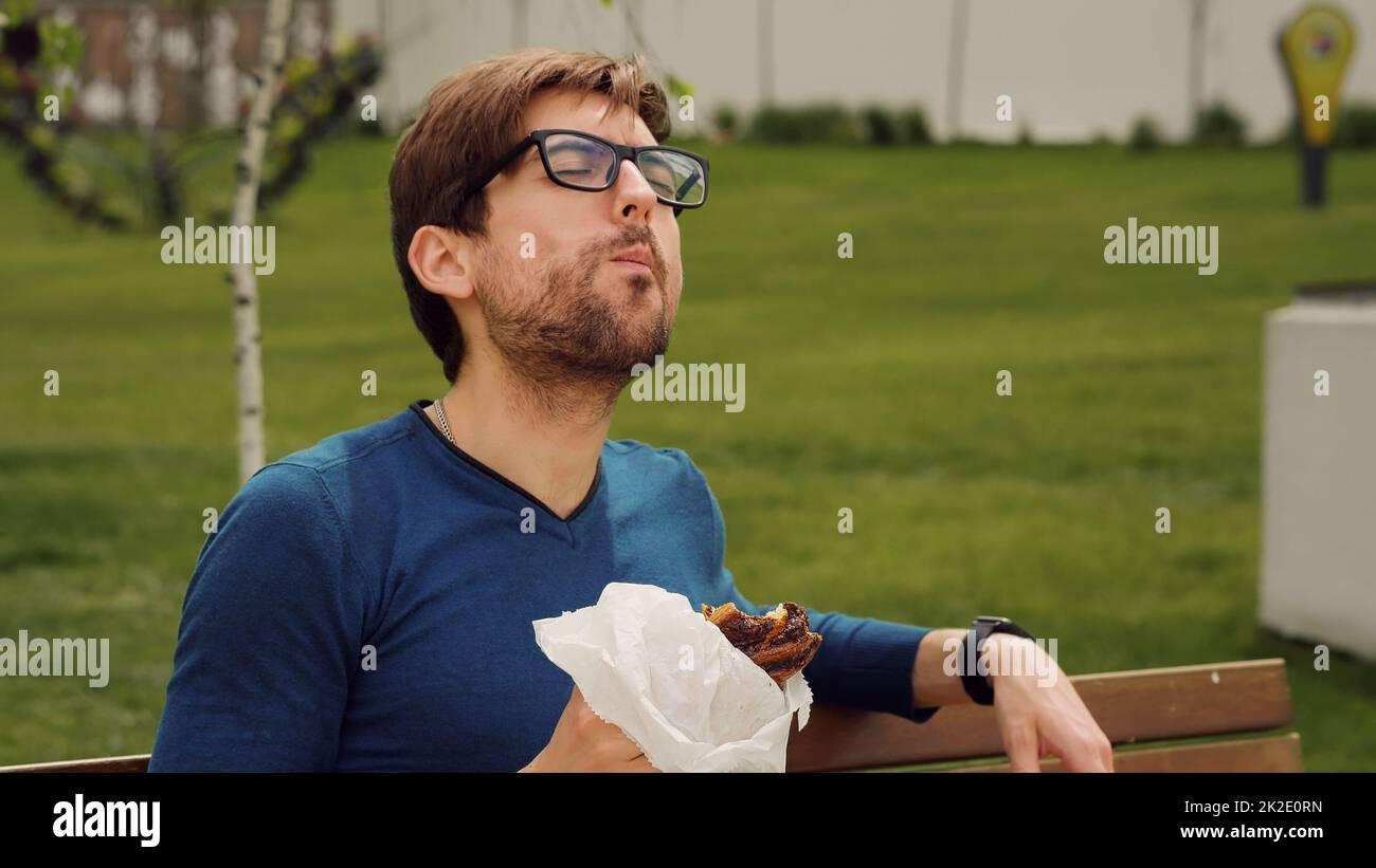 Dipendente che prende lavoro in pausa. Pranzo per giovani che mangia uno spuntino. Bell'uomo che si gode il cibo. Ritratto dell'uomo affamato. Foto Stock