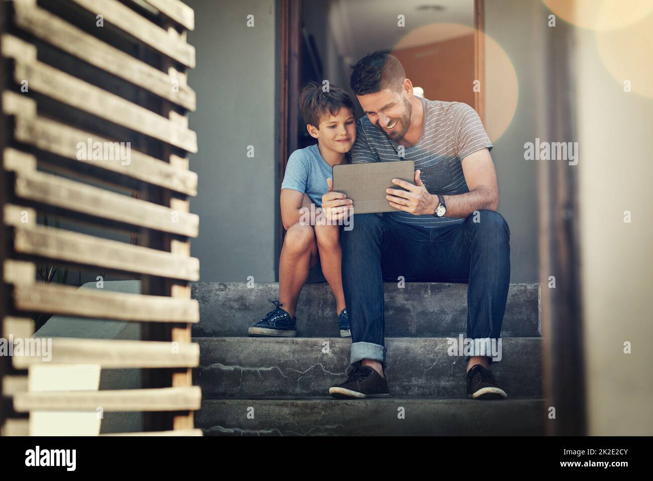 Insegnare al suo piccolo ragazzo un mondo online. Girato da un padre e un figlio usando un tablet digitale insieme sui gradini anteriori della loro casa. Foto Stock