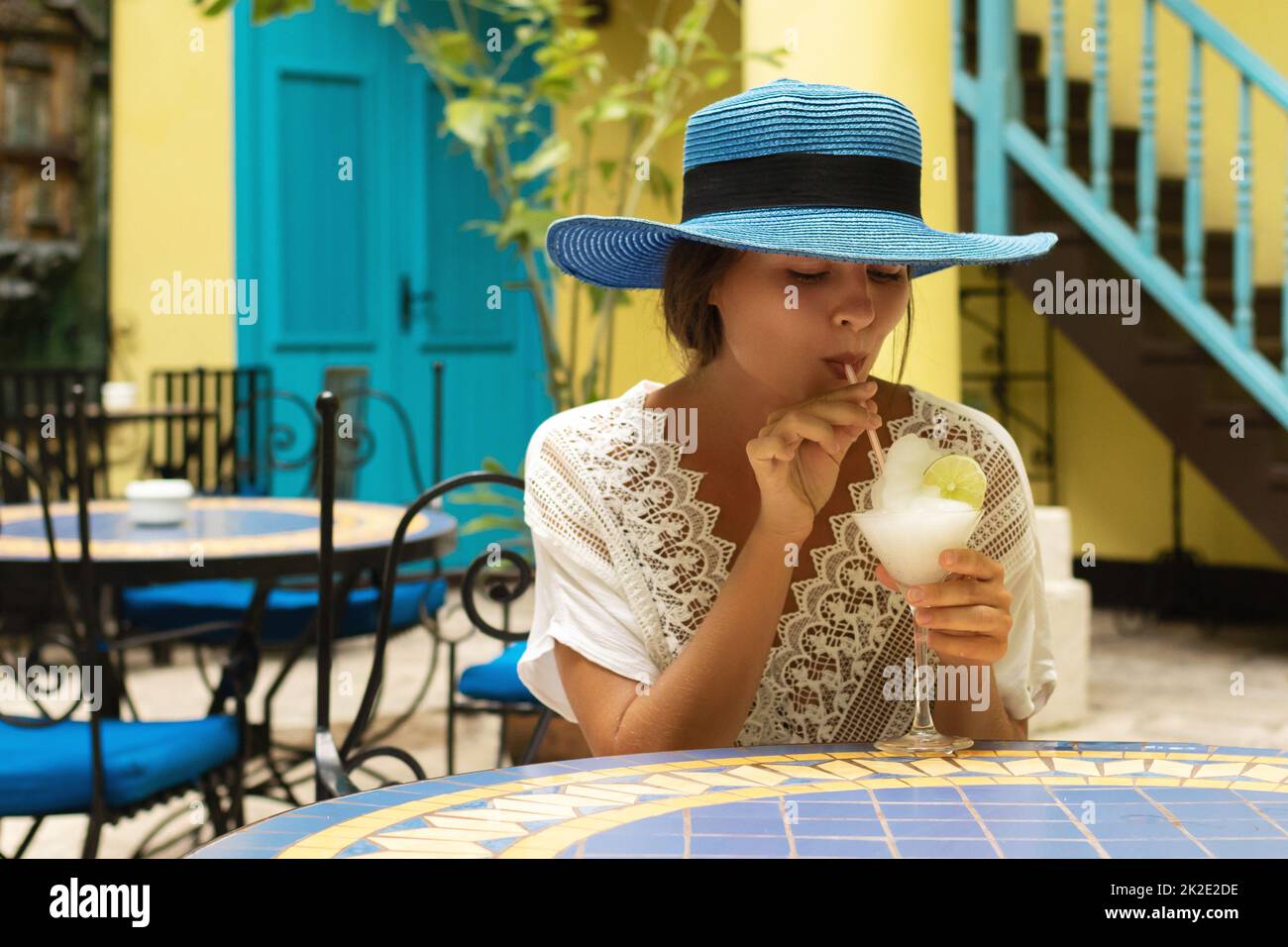 Donna che indossa cappello blu si sta godendo il suo cocktail freddo nel caffè della città Foto Stock
