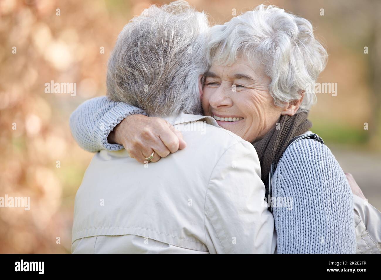 Amicizia thats costruito per durare. Due donne anziane abbracciano con alberi ombreggiati in autunno sullo sfondo. Foto Stock