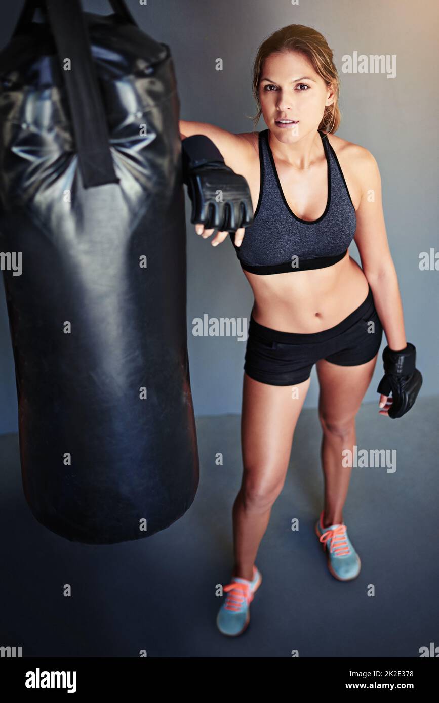 Formazione per diventare in forma di combattimento. Ritratto di un pugile femminile appoggiato a un sacco di punzonatura. Foto Stock