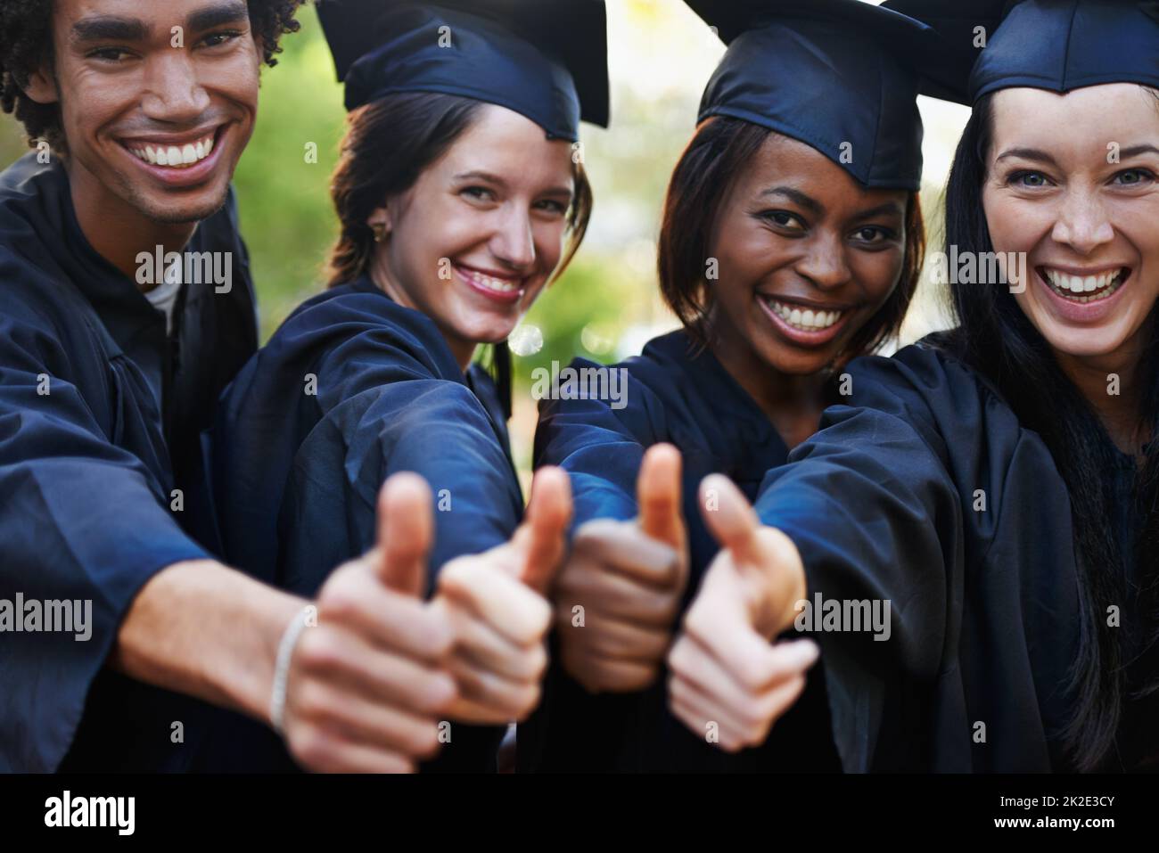Ottieni un'istruzione. Un gruppo di laureati sorridenti che danno i pollici in su alla laurea. Foto Stock