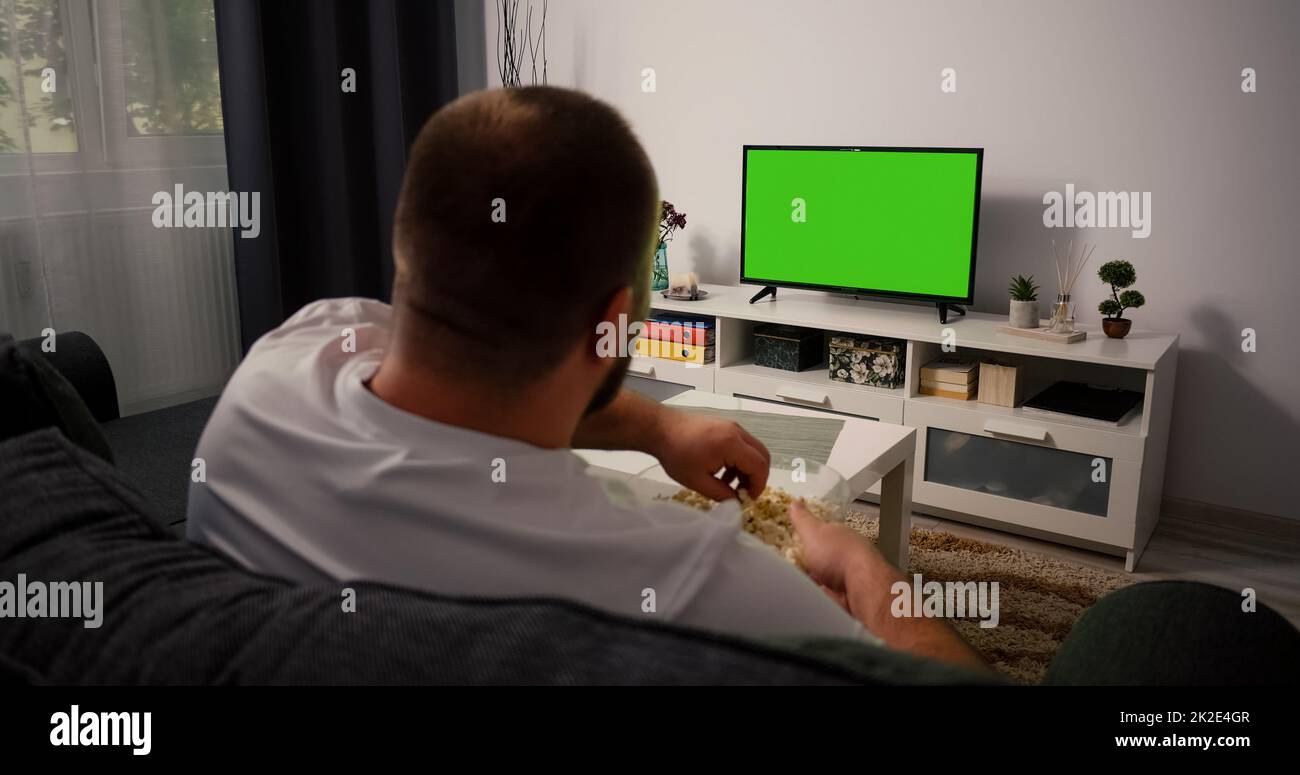 Uomo che guarda TV a schermo verde Chroma Key. Vista posteriore di un uomo di mezza età seduto su un divano rilassante soggiorno in TV. Foto Stock