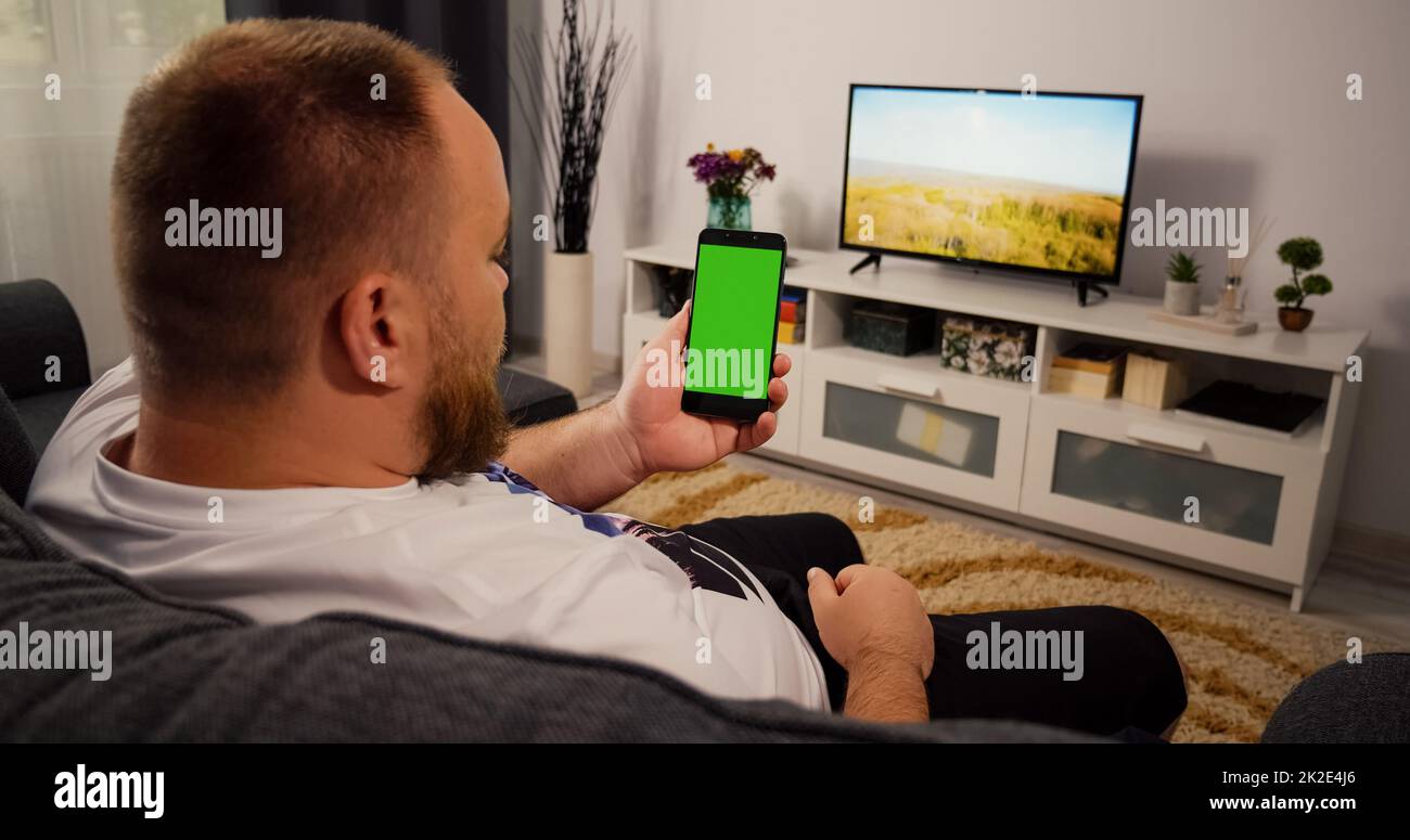Uomo che utilizza smartphone con schermo verde per Copy Space Chroma Key Mockup. Gesti di scorrimento. Maschio guardare gadget schermo verde e touch display. Foto Stock