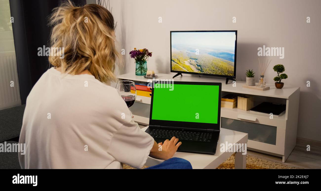 Donna seduta sul divano utilizzando un notebook con Greenscreen e Chroma  Key. Simulate con i marcatori di tracking e Alpha Matte. Donna caucasica  rilassarsi la sera su un computer portatile e bere