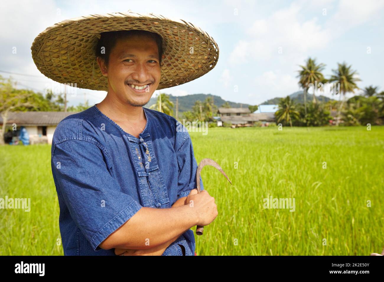 Tempo di raccolta quasi. Ritratto di un coltivatore di riso che detiene un tradizionale strumento di raccolta - Thailandia. Foto Stock