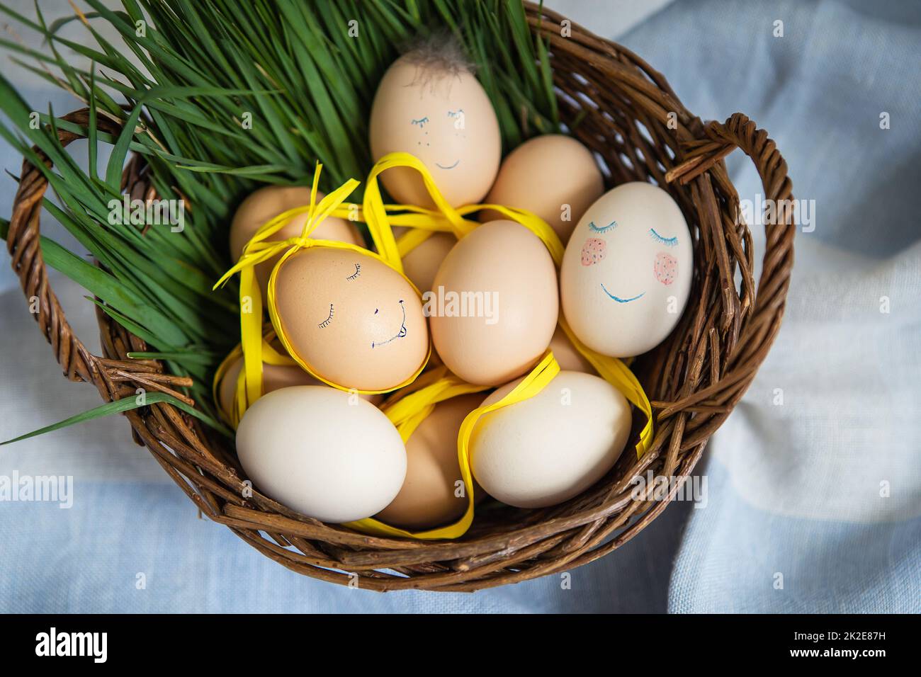 Belle uova di Pasqua dipinte con un viso carino, che giacciono in un cesto di legno insieme all'erba verde. Cartolina di Pasqua. Foto Stock
