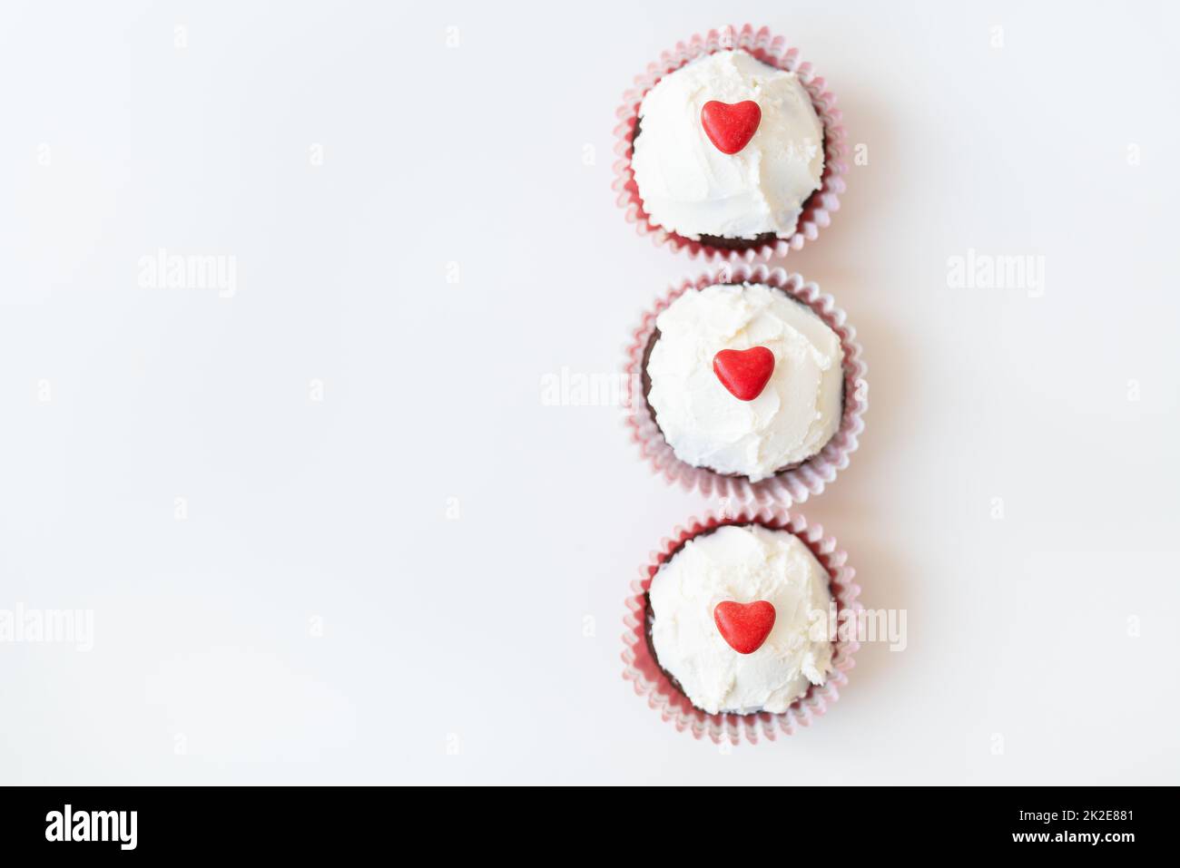 San Valentino-14 febbraio. Muffin al cioccolato dolce con crema al burro e cuore rosso per la decorazione su sfondo bianco. Foto Stock