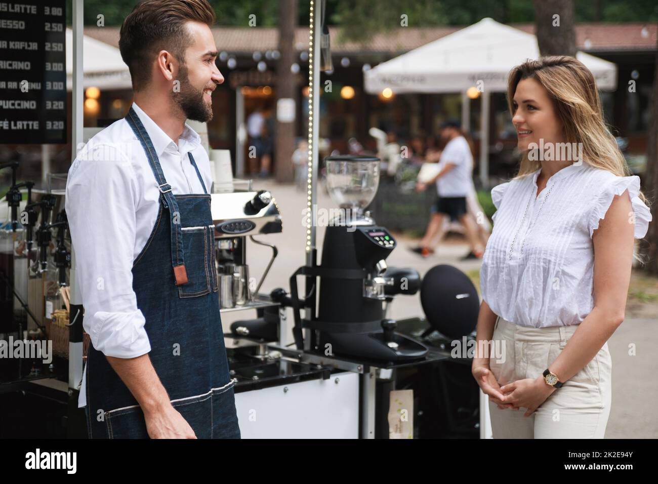 L'uomo barista e la sua donna cliente hanno una piccola conversazione durante la giornata estiva accanto al bar. Foto Stock