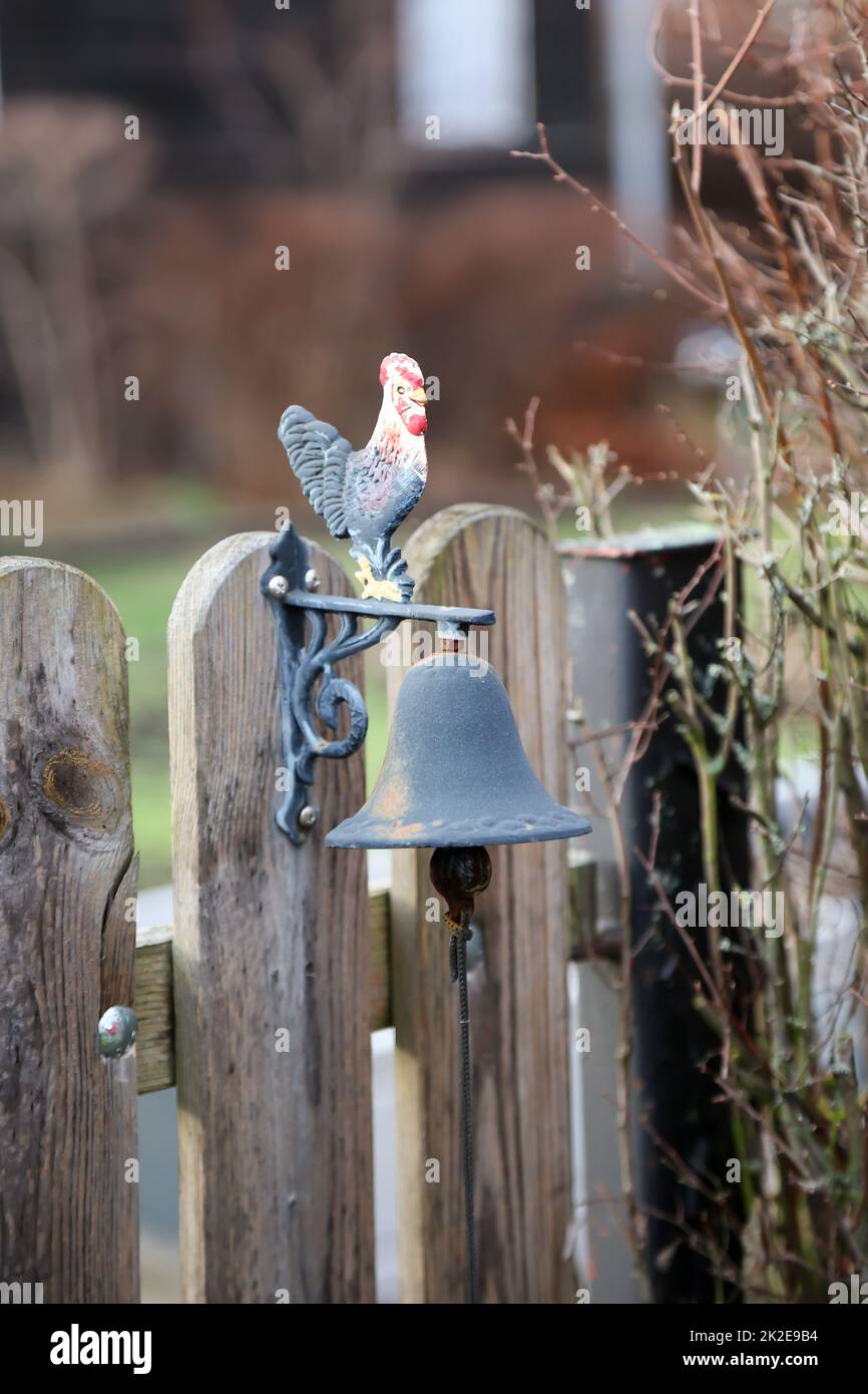 Una campana con un gallo su un cancello del giardino. Foto Stock