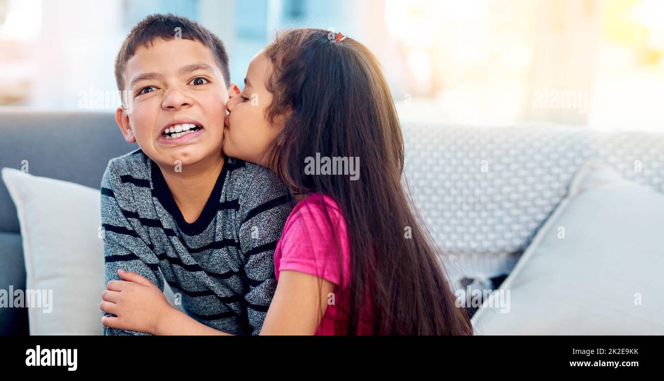 Yuck, le ragazze sono bizzarre. Scatto di una bambina adorabile baciando il suo fratello maggiore sulla guancia a casa. Foto Stock