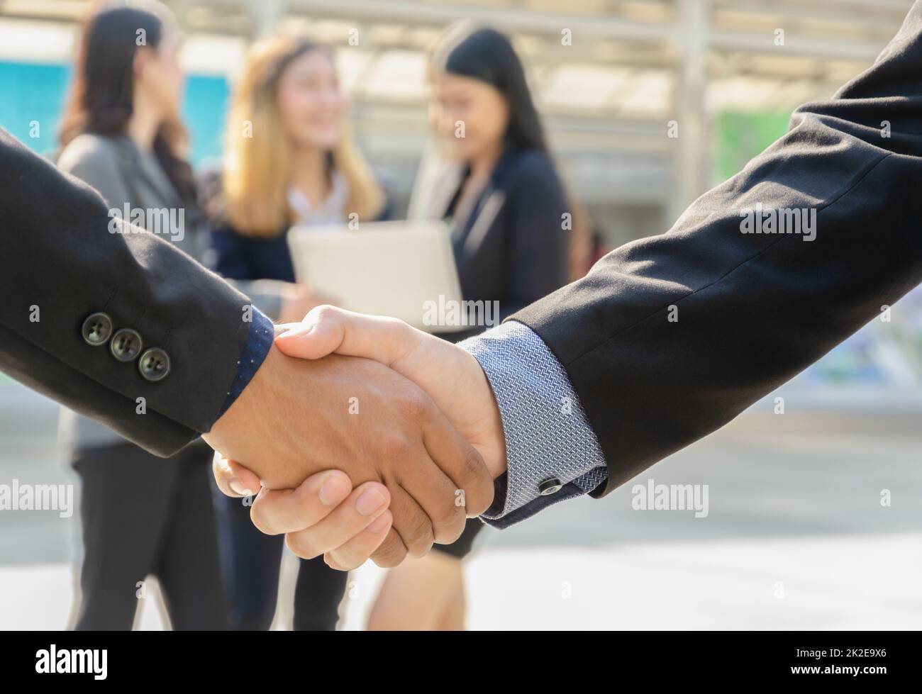 Due uomini d'affari che scuotono le mani davanti al loro team aziendale in piedi all'aperto. Foto Stock