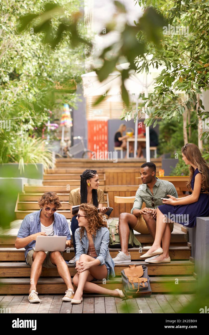 Raffreddamento nel campus tra le classi. Un gruppo di giovani studenti che si rilassano all'aperto con dispositivi tecnologici. Foto Stock