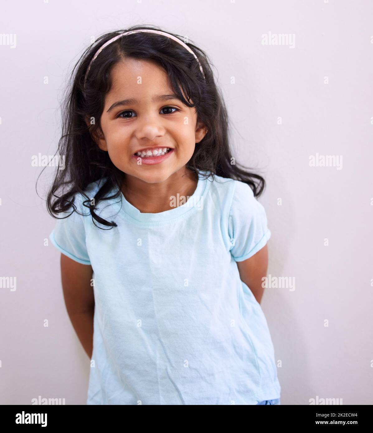 Basta guardare quel sorriso adorabile. Scatto ritagliato di una bambina adorabile che si posa contro un muro. Foto Stock