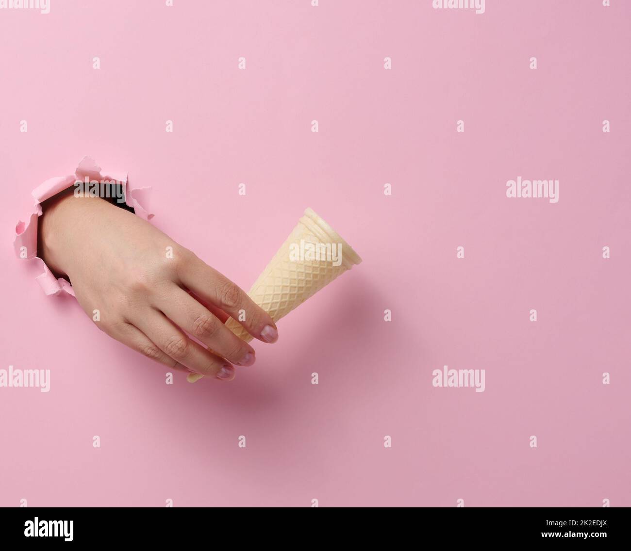 svuotate la tazza con il cono per il gelato in una mano della donna che si stacca da un foro strappato in una carta rosa Foto Stock